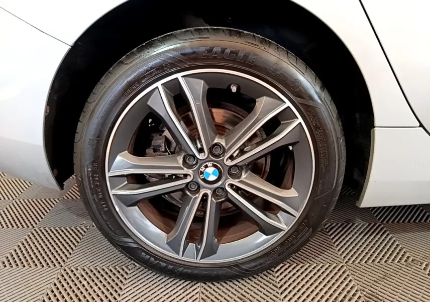 Gros plan sur la roue avant droite d'une BMW Série 1 gris clair avec jante alliage à 5 doubles branches.