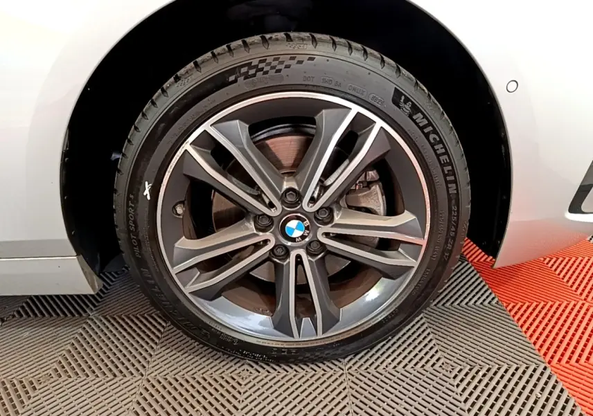 Gros plan sur la roue avant droite avec jante alliage gris et logo BMW sur une BMW Série 1 gris clair.