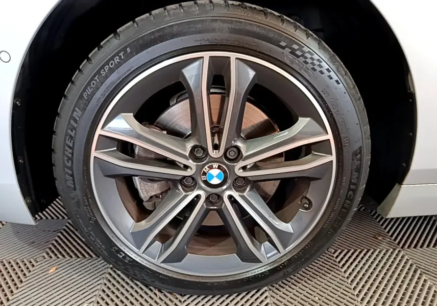 Gros plan sur la roue avant droite gris clair d'une BMW Série 1 118i Edition Sport avec jante alliage et logo BMW central.