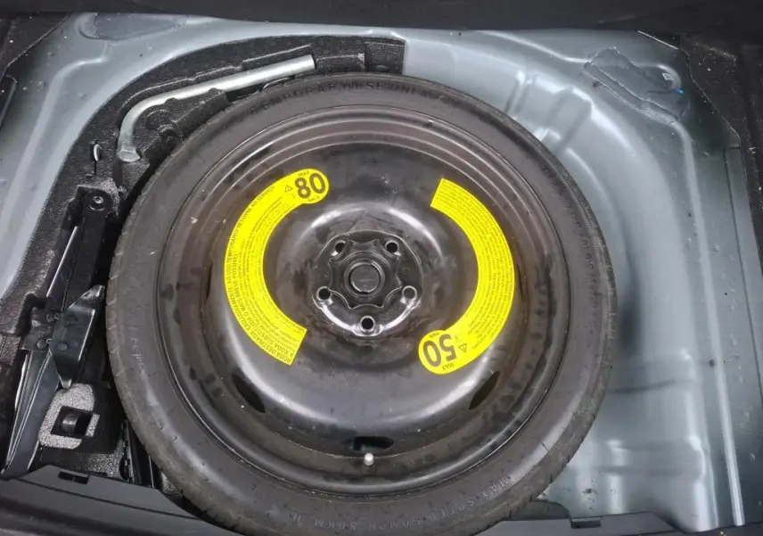 Vue rapprochée de la roue de secours noire avec étiquettes jaunes dans le coffre d’une SEAT Leon gris 2021.