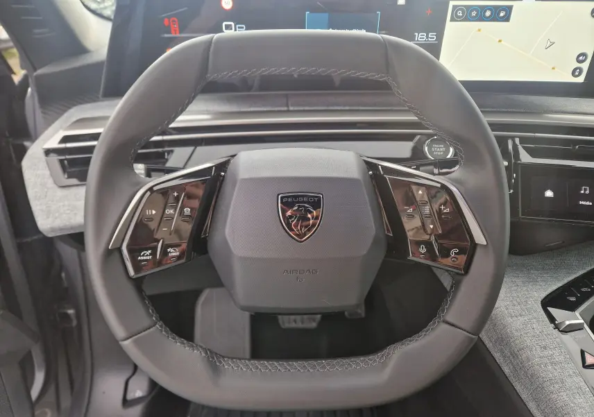 Vue rapprochée du volant cuir noir du Peugeot 3008 2025 avec commandes intégrées et écran panoramique en arrière-plan.