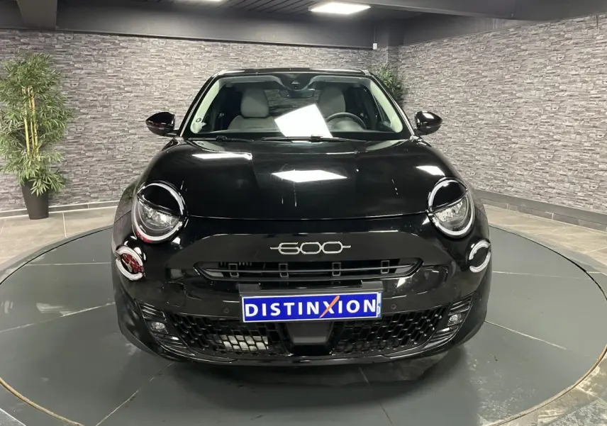 Vue frontale d'une FIAT 600 noire 2024 avec logo 600 chromé et calandre noire brillante en intérieur showroom.