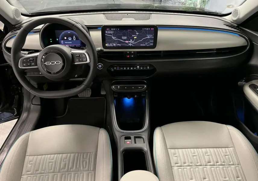 Intérieur de la FIAT 600 hybride 2024 vu de face, avec sellerie ivoire et tableau de bord moderne éclairé bleu.
