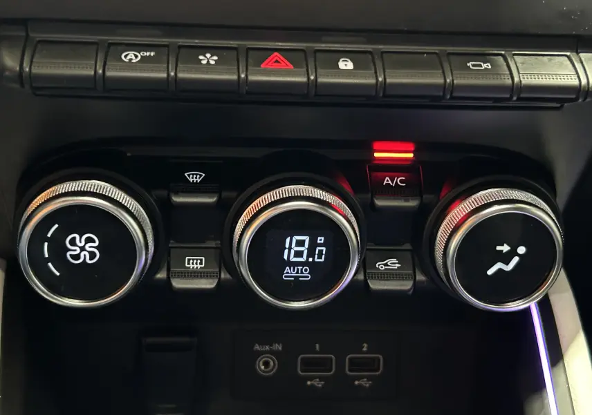 Gros plan sur la console centrale de la Renault Clio V rouge 2023, montrant les commandes de climatisation et boutons fonctionnels.
