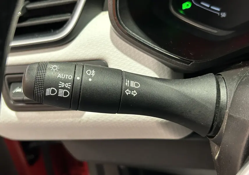 Gros plan sur la commande des feux et clignotants à gauche du volant dans l'habitacle d'une Renault Clio V rouge.