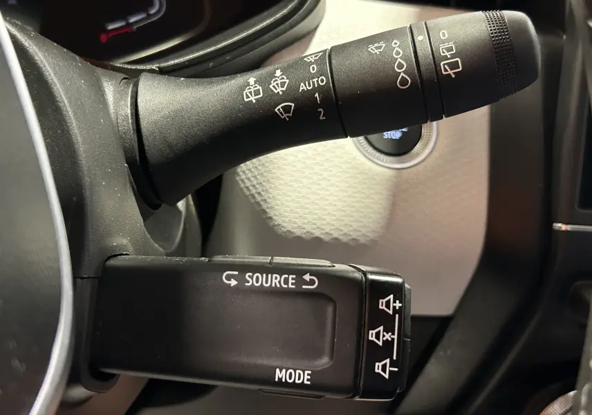 Gros plan sur les commandes au volant de la Renault Clio V rouge 2023, avec bouton source et réglages essuie-glace visibles.