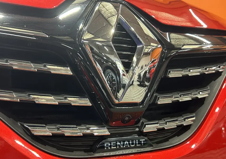 Gros plan sur la calandre rouge d'une Renault Clio V TCe 90 TECHNO avec logo chromé et caméra 360° intégrée.