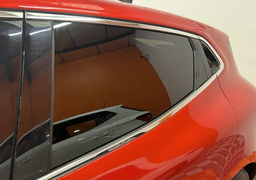 Gros plan sur la partie arrière droite d'une Renault Clio V rouge 2023 avec vitres teintées et contours chromés.