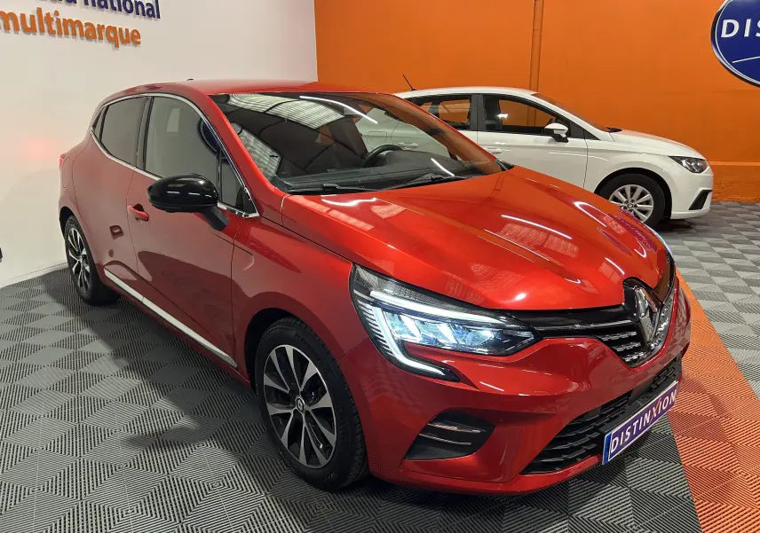 Vue 3/4 avant d'une Renault Clio V TCe 90 TECHNO rouge avec phares LED allumés et rétroviseurs noirs.