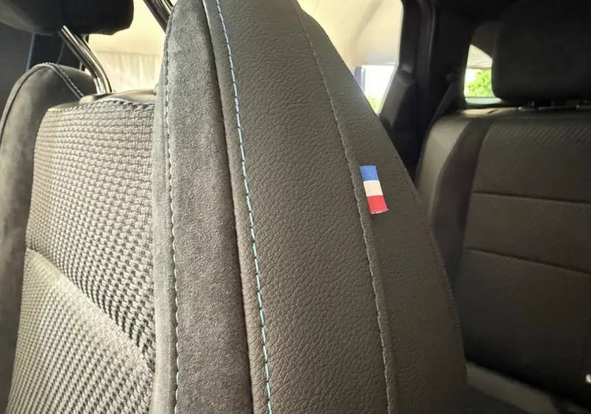 Gros plan sur la couture bleue et le drapeau tricolore du siège avant côté gauche du Renault Espace gris foncé esprit Alpine.