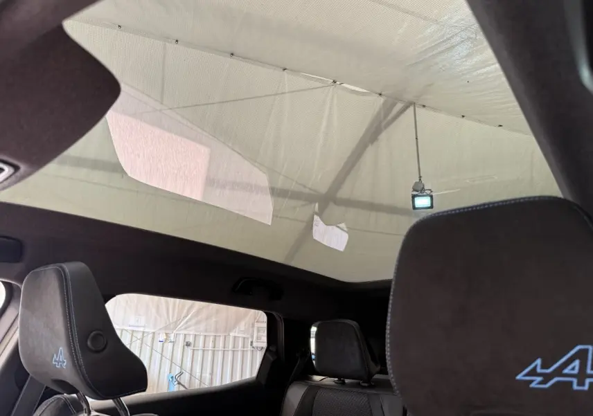 Vue intérieure arrière montrant les appuis-tête noirs avec logo Alpine bleu et toit panoramique du Renault Espace gris foncé esprit Alpine.