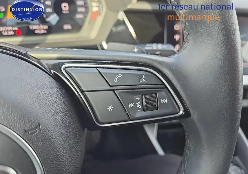 Gros plan sur les commandes au volant cuir noir de l’Audi A3 Sportback gris Daytona, avec palettes au volant visibles.