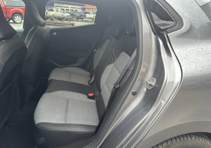 Vue côté droit sur la banquette arrière gris clair et noir de la Renault Clio gris schiste 2025 avec portière ouverte sous la pluie.