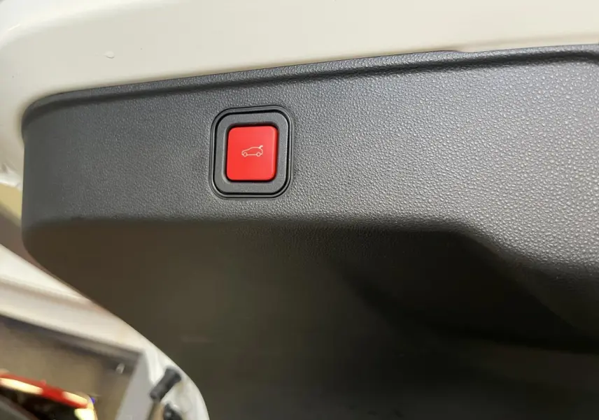 Bouton rouge d'ouverture électrique du hayon sur le bord intérieur du coffre d'une FIAT 600 blanche 2024.