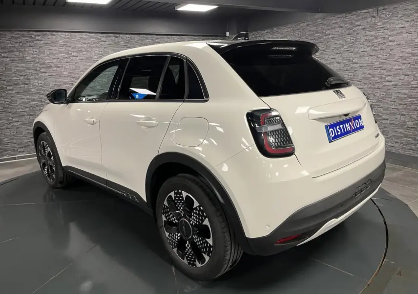 Vue 3/4 arrière droite d'une FIAT 600 blanche avec jantes alliage noires et toit noir brillant en intérieur showroom.