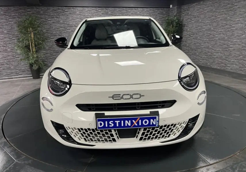 Vue frontale d'une FIAT 600 blanche avec logo chromé 600 et calandre ajourée dans un showroom.