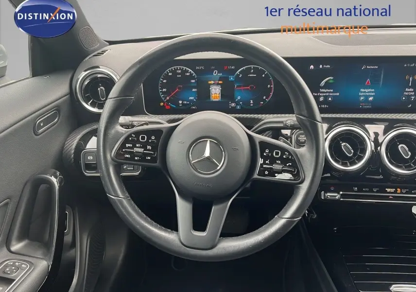 Vue frontale du tableau de bord et du volant en cuir noir d'une Mercedes CLA Shooting Brake 180 argent iridium, avec écran numérique et aérateurs ronds chromés.