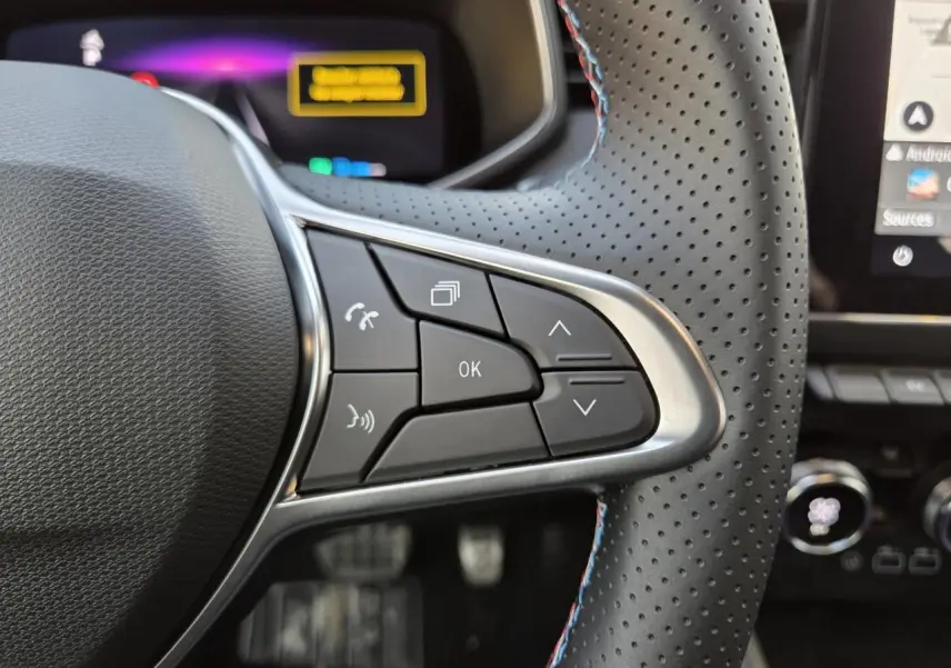 Gros plan sur les commandes du volant perforé avec surpiqûres tricolores de la Renault Clio V hybride Gris Rafale.