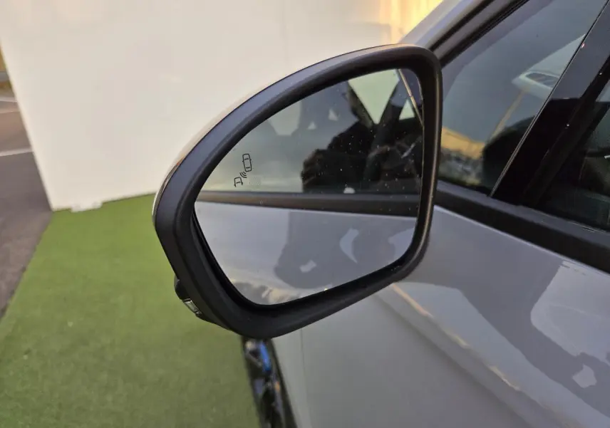 Rétroviseur côté gauche de la Renault Clio V hybride gris Rafale avec indicateur d'angle mort visible.