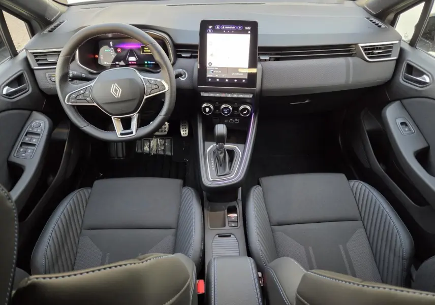 Vue intérieure avant de la Renault Clio V hybride 2025, sièges noirs avec surpiqûres bleues et écran tactile vertical.