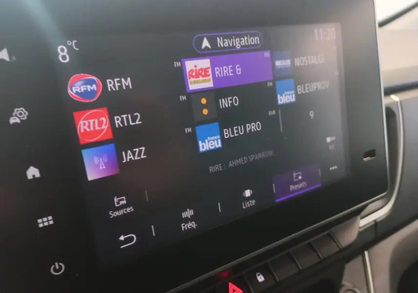 Écran tactile central du tableau de bord du Renault Trafic Fourgon blanc, affichant les stations radio et la navigation.