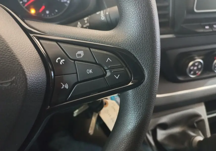 Gros plan sur les commandes multifonctions du volant noir du Renault Trafic Fourgon blanc, avec tableau de bord en arrière-plan.