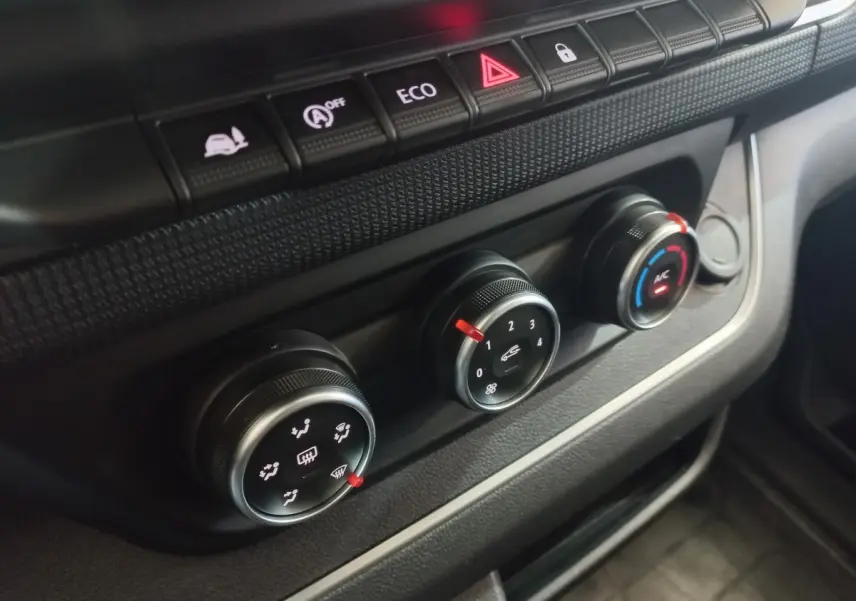 Gros plan sur les commandes de climatisation et boutons de fonction du tableau de bord du Renault Trafic Fourgon blanc.