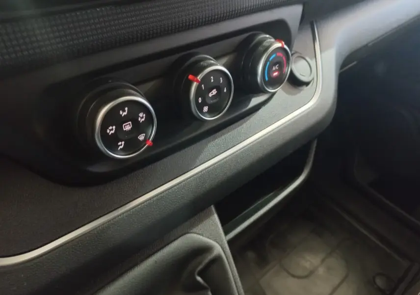 Gros plan sur les commandes de climatisation noires du tableau de bord du Renault Trafic Fourgon blanc, version 2022.