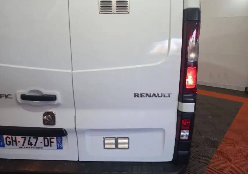 Vue arrière droite du Renault Trafic Fourgon blanc avec feux arrière allumés et logo visible sur la porte.
