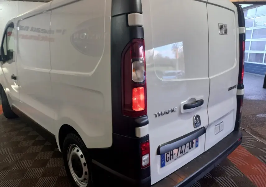 Vue 3/4 arrière gauche d'un Renault Trafic Fourgon blanc avec feux arrière allumés et plaque d'immatriculation française.