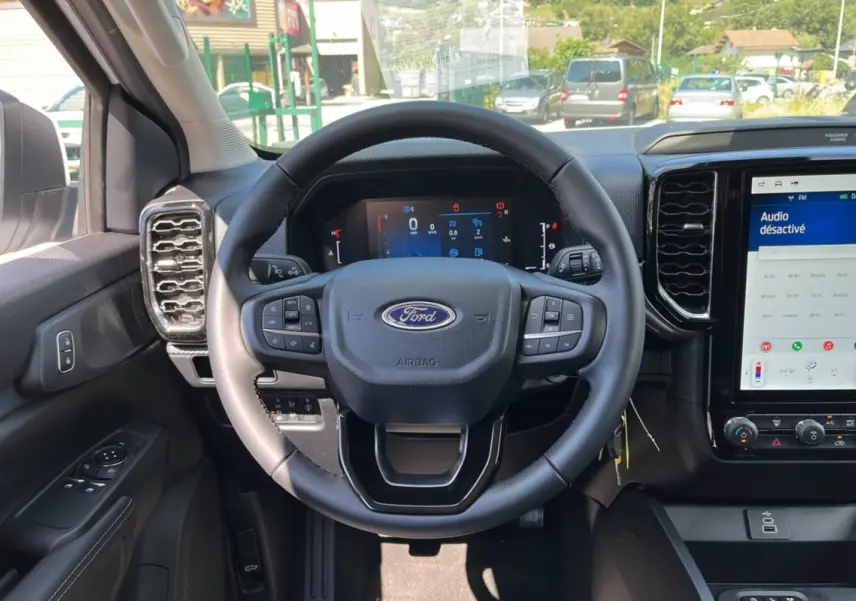 Vue intérieure centrée sur le volant cuir multifonctions du Ford Ranger 2025, avec écran tactile et tableau de bord numérique.