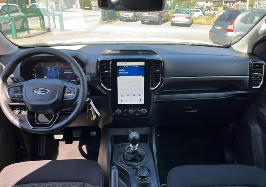 Vue intérieure avant du Ford Ranger 2025 blanc glacier, volant cuir multifonctions et écran tactile vertical central.