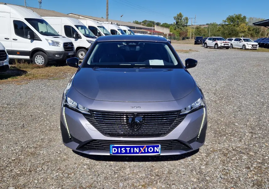 Vue avant d'une Peugeot 308 1.2 Hybrid 145 gris Artense avec calandre noire et feux LED verticaux allumés.