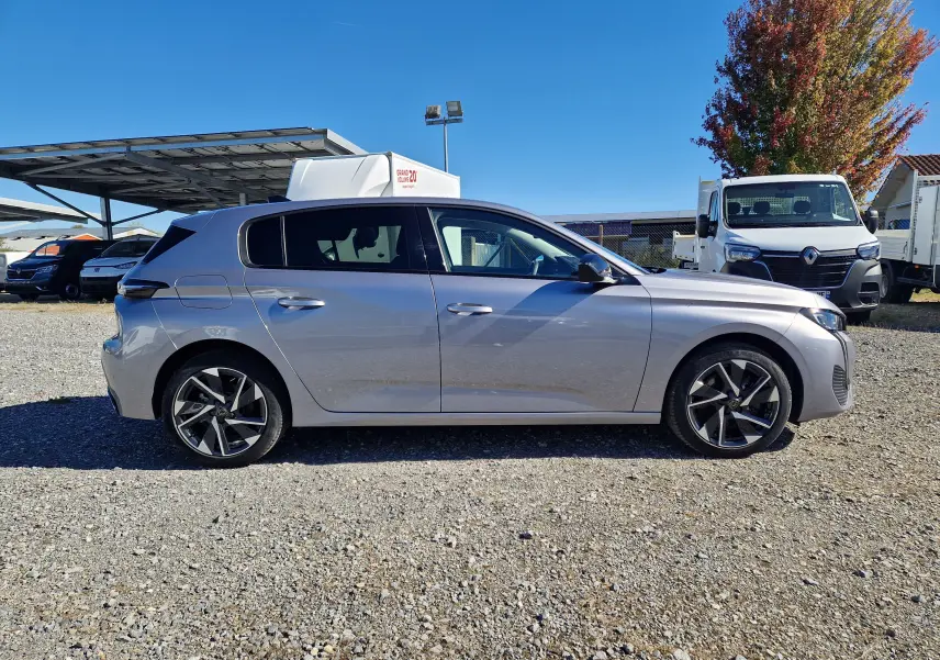 Peugeot 308 1.2 Hybrid 145 en gris Artense vue de profil côté gauche sur un sol gravillonné, avec jantes alliage.