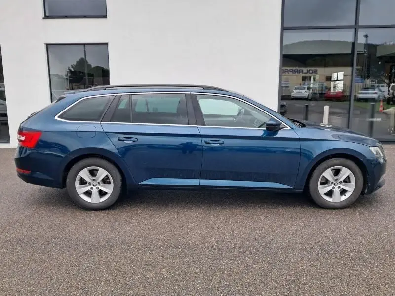 Vue de profil côté gauche d'une Skoda Superb Combi bleu métal de 2018 avec jantes alliage et toit ouvrant.