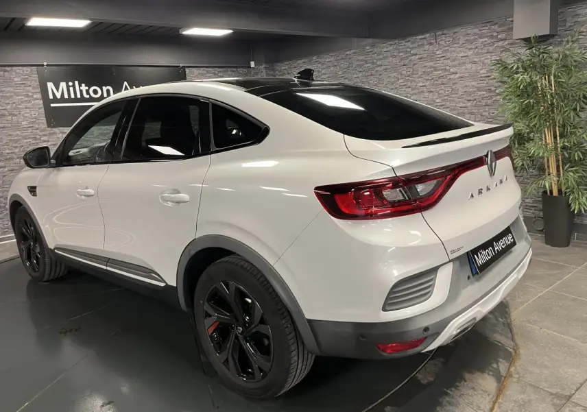 Vue 3/4 arrière droite d'une Renault Arkana blanche avec toit noir brillant et jantes noires R.S. Line dans un showroom.