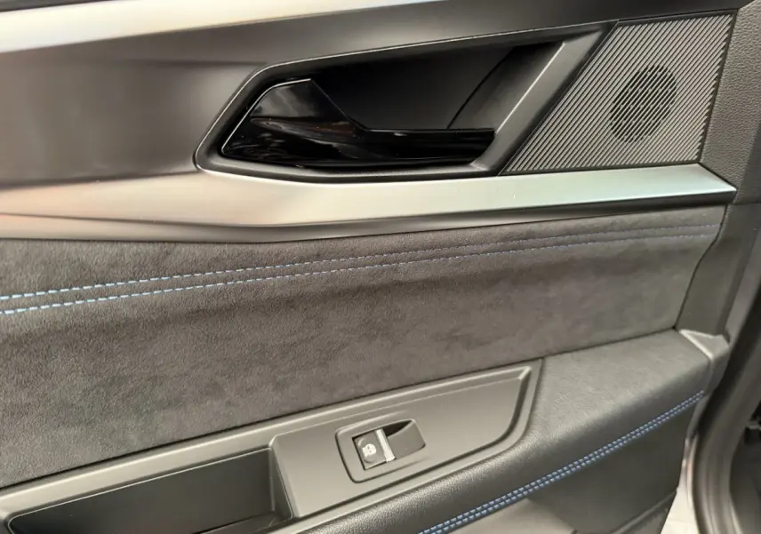 Gros plan sur la porte côté gauche du Renault Espace gris foncé esprit Alpine, avec surpiqûres bleues et poignée noire brillante.