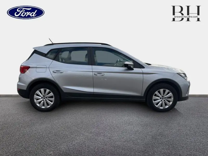 Vue de profil côté gauche d'un SEAT ARONA gris urbain métal avec barres de toit et jantes alu.