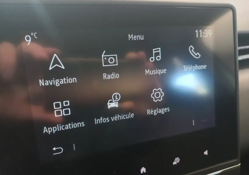 Écran tactile central de la Renault Clio Business blanc, affichant le menu principal avec navigation et musique.