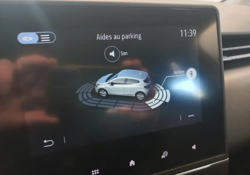 Affichage tactile intérieur montrant l'aide au parking avec vue 3D d'une Renault Clio blanche de profil côté gauche.
