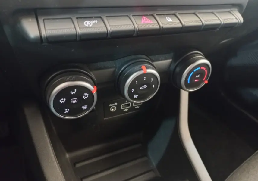 Gros plan sur les commandes de climatisation et ventilation noires de la Renault Clio Business blanche, avec boutons rotatifs et ports USB.