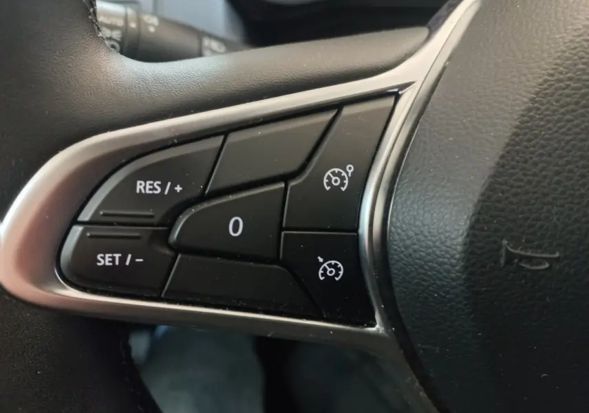 Gros plan sur les commandes de régulateur de vitesse à gauche du volant cuir noir de la Renault Clio Business blanche 2021.