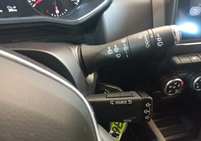 Gros plan sur les commandes au volant noir de la Renault Clio Business blanche, avec tableau de bord et boutons de climatisation visibles.