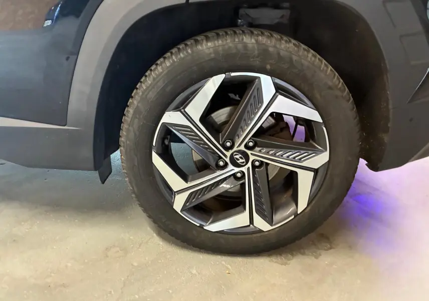 Gros plan sur la roue avant gauche du Hyundai Tucson noir 2022, mettant en valeur la jante alliage au design moderne.