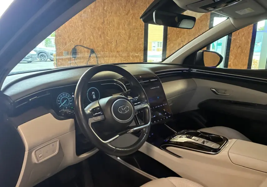 Vue intérieure côté conducteur du Hyundai Tucson 2022 hybride, avec tableau de bord numérique et sellerie beige.