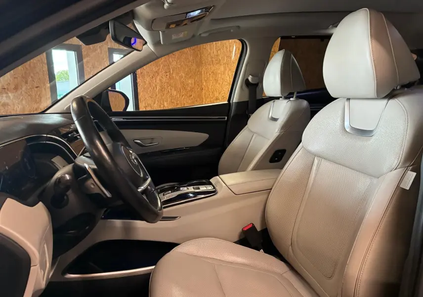 Vue intérieure côté conducteur du Hyundai Tucson 2022, sièges en cuir beige et tableau de bord noir élégant.