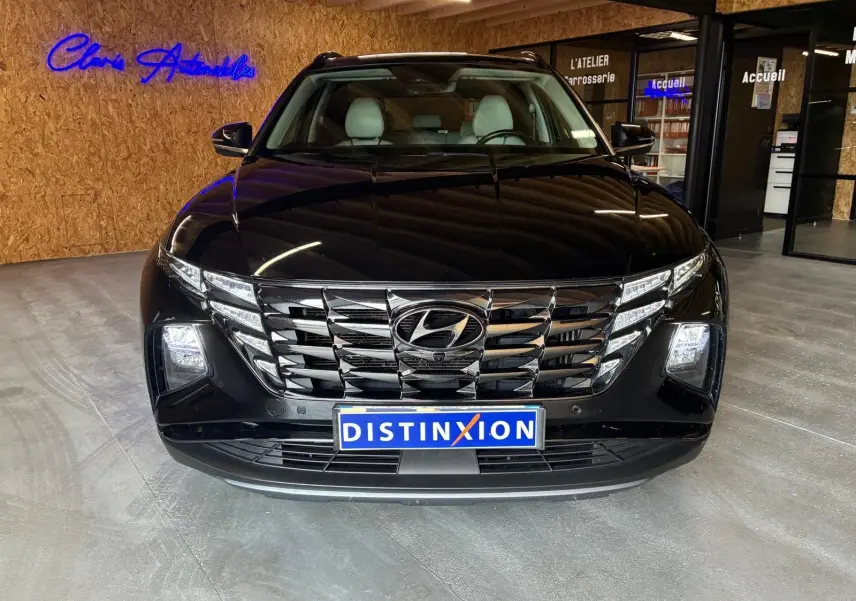 Vue avant d’un Hyundai Tucson noir 2022 avec calandre chromée et phares LED allumés en intérieur showroom.