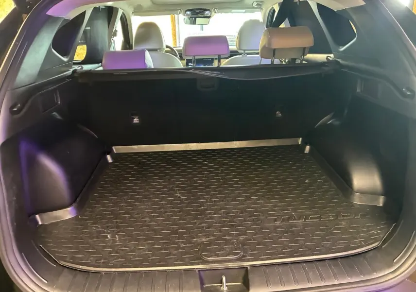 Vue intérieure du coffre ouvert d'un Hyundai Tucson noir 2022, montrant le tapis de coffre et les sièges arrière beiges.