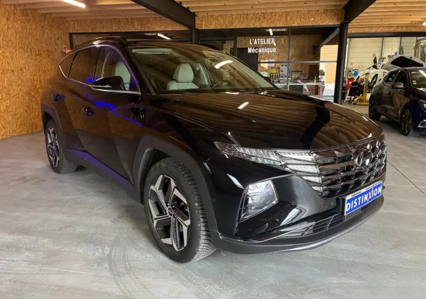 Vue 3/4 avant droite du Hyundai Tucson noir 2022, soulignant sa calandre distinctive et ses jantes modernes en intérieur d'atelier.