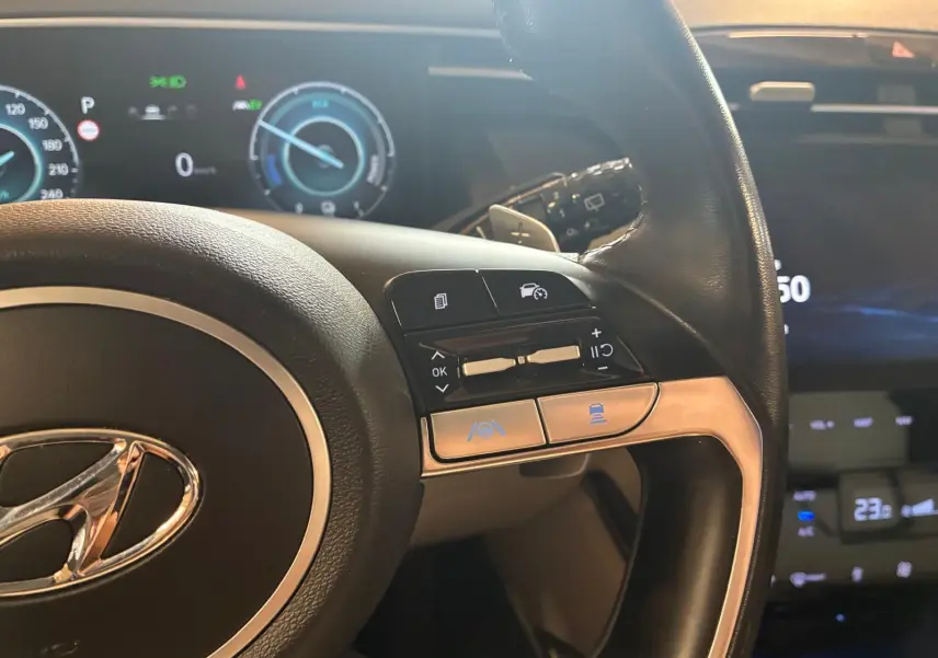 Gros plan sur le volant noir du Hyundai Tucson 2022 avec commandes intégrées et tableau de bord numérique en arrière-plan.